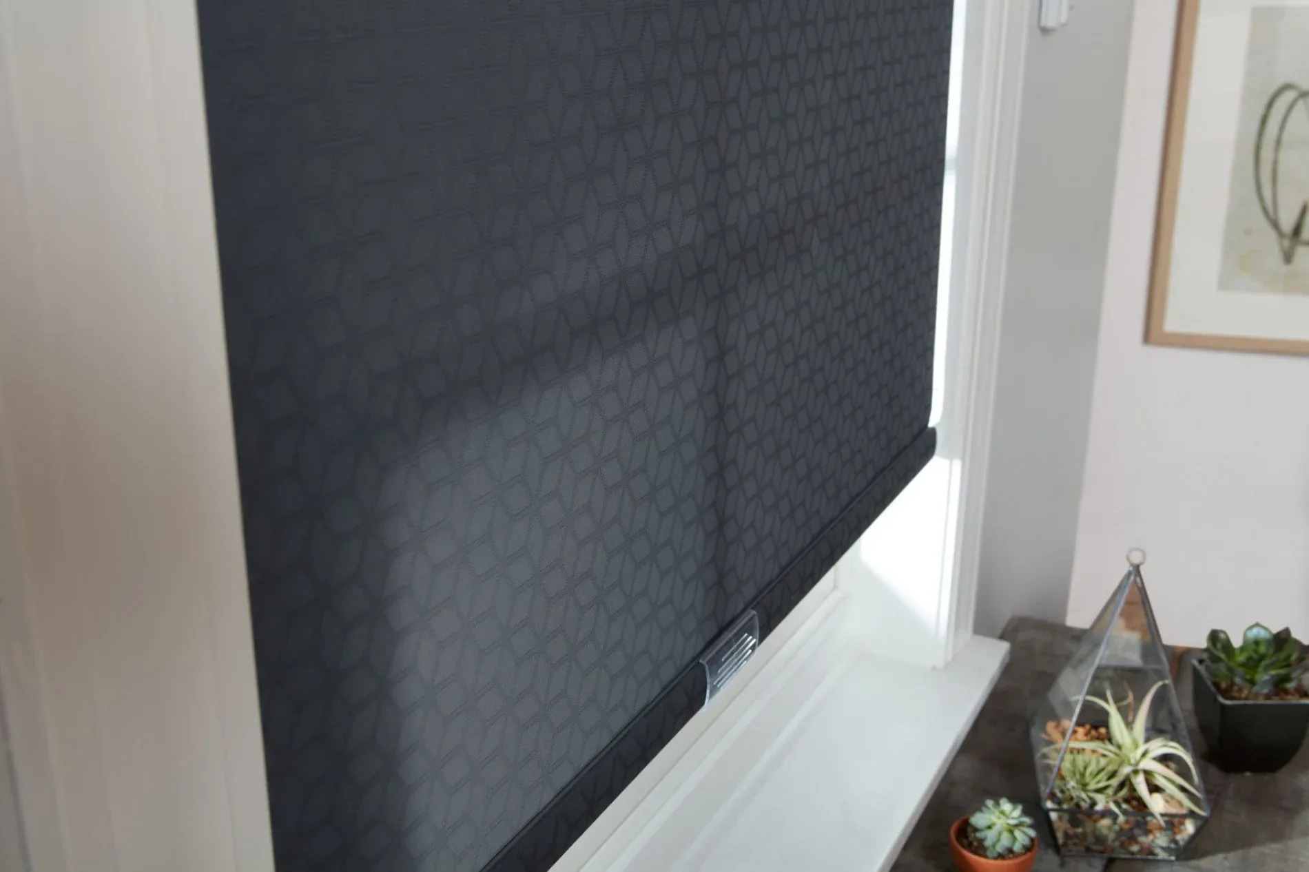 An image showing the inside of a white-walled room, with a window on the left-hand wall. The window has a black roller shade with a star pattern, and it is pulled almost all the way down to cover much of the glass.