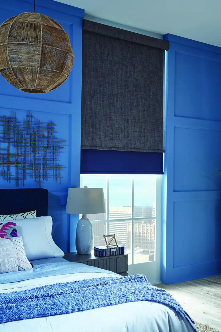 A room with blue walls and a denim-colored roller shade over the window