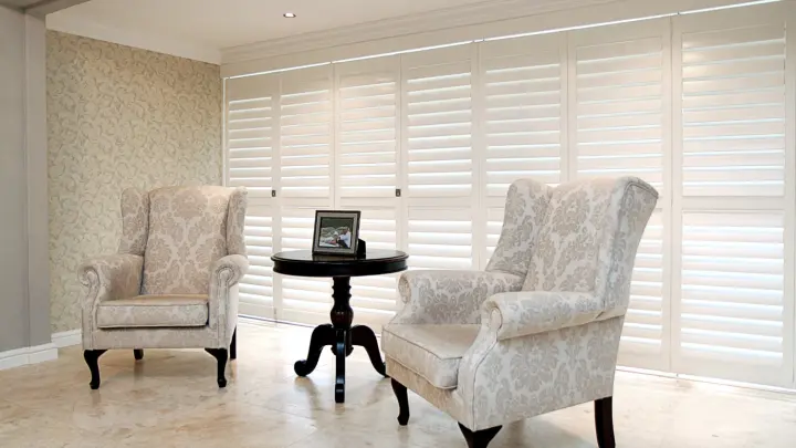 Seating area with beautiful white furniture and large window shutters on giant window behind them