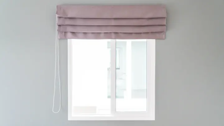 A window with a pink shade with multiple folds in it