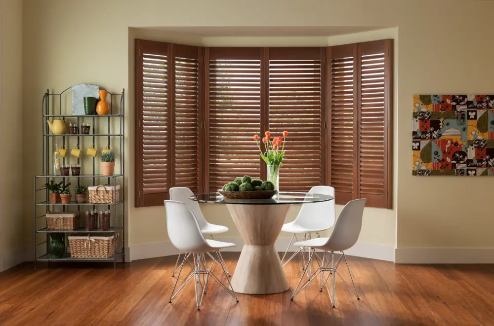 An image of a dining room featuring rich wood indoor shutters in a bay window.