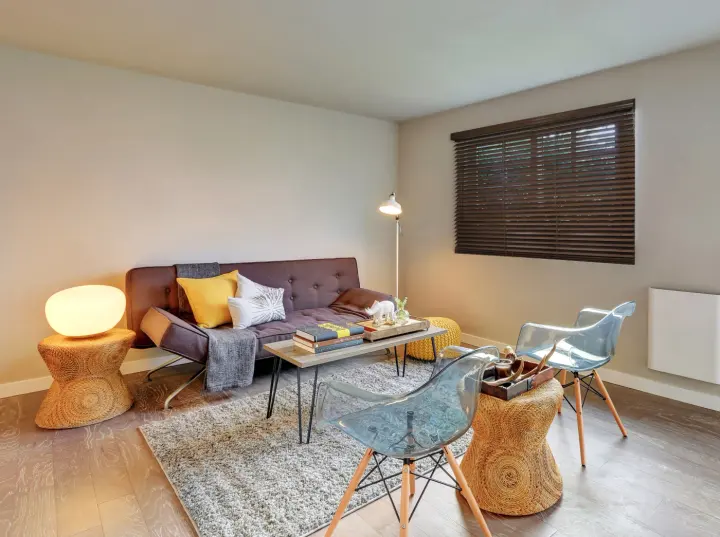 A sitting room with a brown couch and brown wood blinds covering the window.