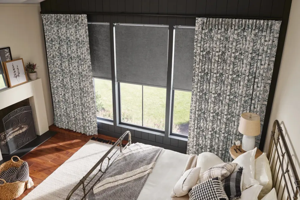 Gray patterned drapery layered over gray shades in a bedroom.