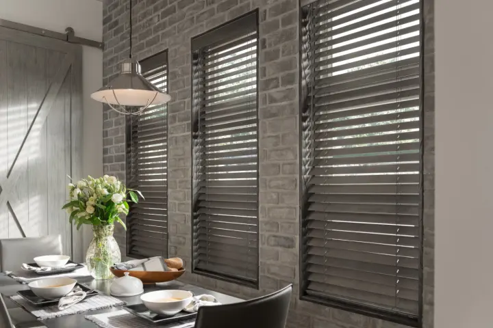 Close-up of wood blinds covering three windows in a brick wall.
