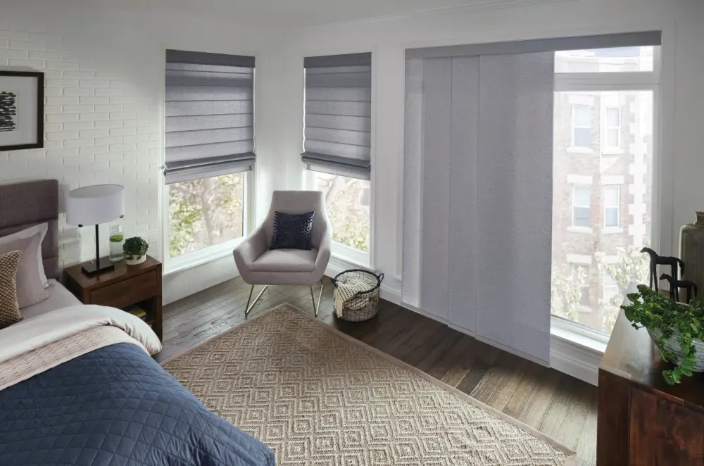 A sitting room with a chair in the corner and gray motorized shades on the windows.