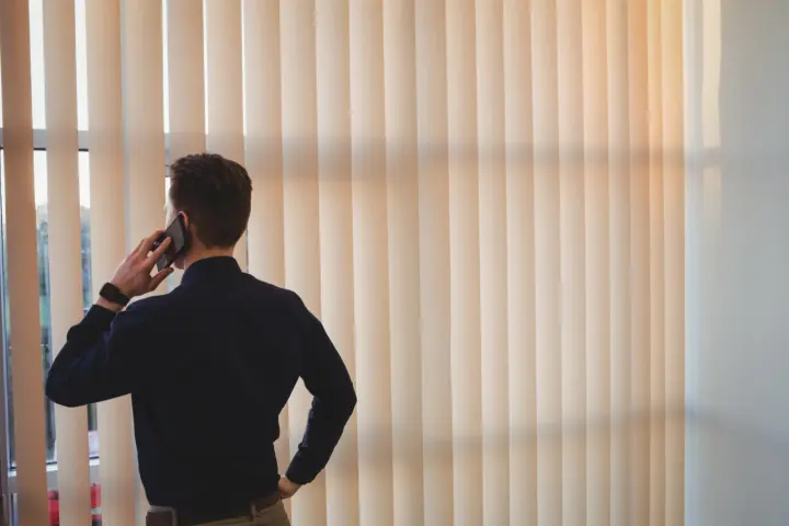 Man taking business call in Las Vegas office with vertical blinds | Southwest Blinds and Shutters