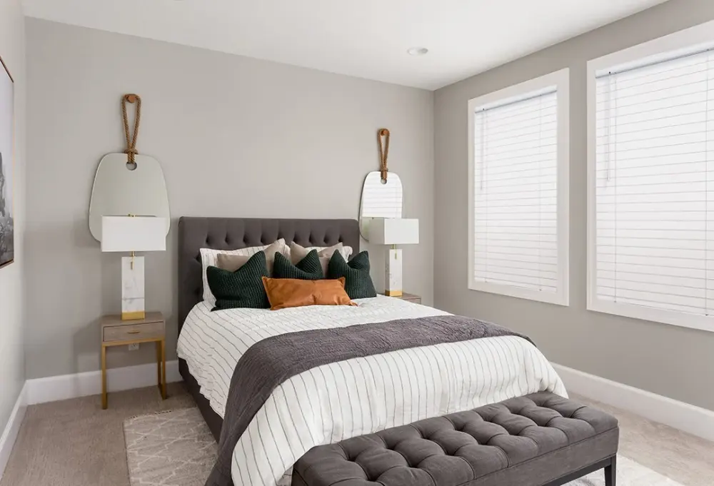 Modern bedroom with custom white faux wood blinds, upholstered bed, neutral décor, and layered bedding .