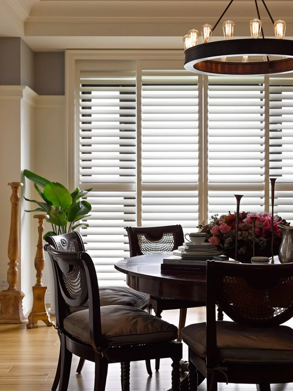 A dining room with elegant decor and white interior shutters covering the windows