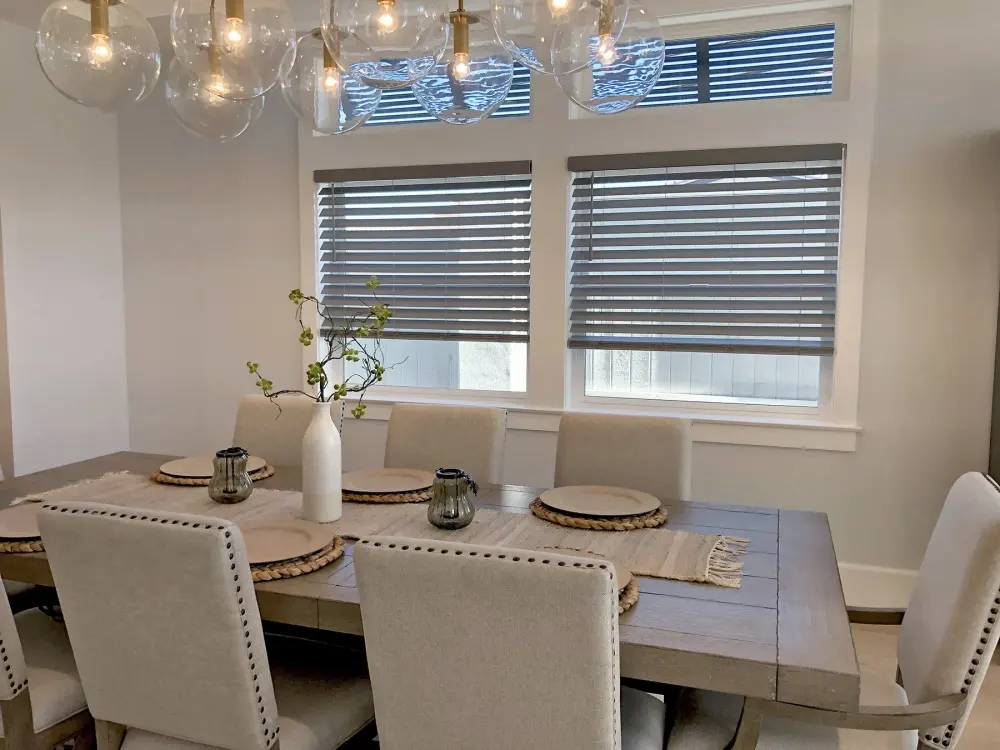 Elegant living room with custom window blinds, large sunlit windows, stylish furnishings, warm neutral décor, and refined light control.