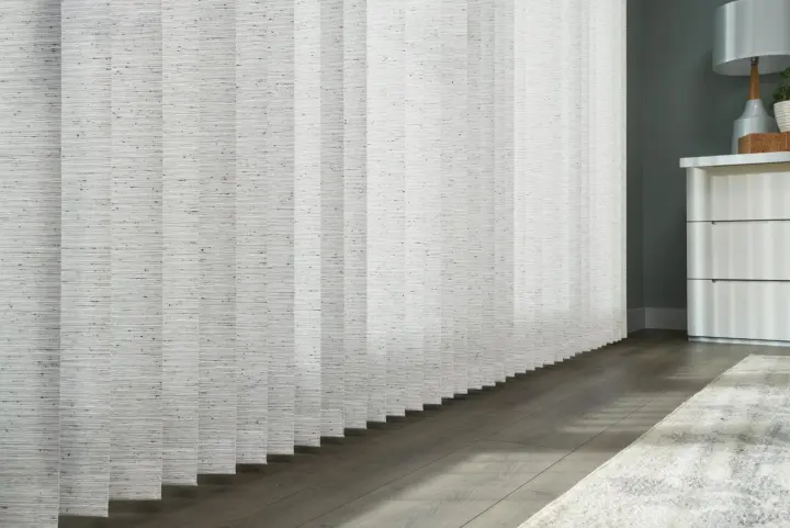 A light gray vertical blinds in a modern room with wood floors, a white cabinet, and a soft area rug.