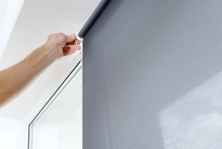Gray roller window shade on a window with a man’s hand adjusting it