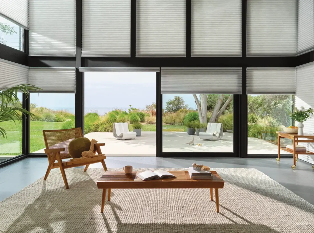 Cellular motorized shades on windows in a large living room with a wood table and chair