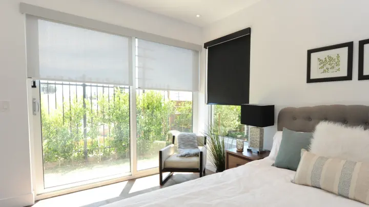 Home bedroom with two tall windows with newly installed roller window shades on them