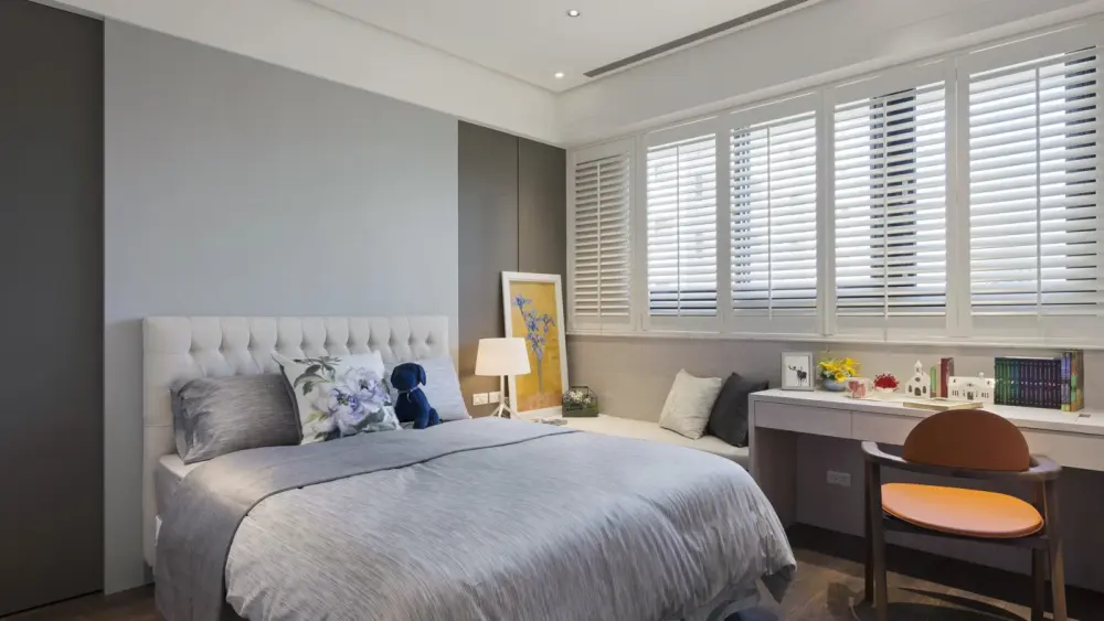 Home bedroom with white shutters on the windows above a cozy bed