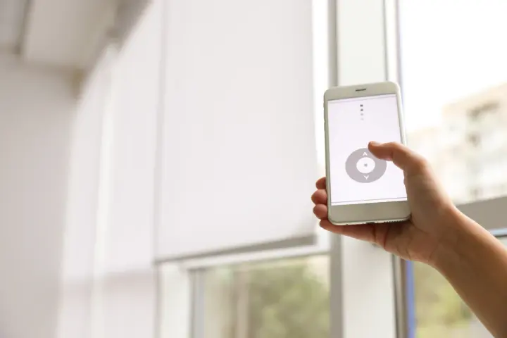 Close-up of a phone controlling crisp, white motorized shades behind it