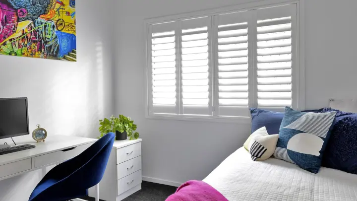 Bedroom with white interior, desktop computer sitting on white desk, small white drawer, white half-closed shutters