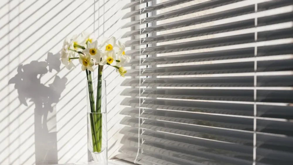 Close-up side view of light gray window blinds containing yellow flowers
