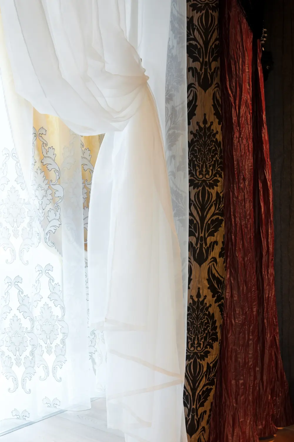 A close-up of multi-layered drapery that are white, red, and gold with a pattern.