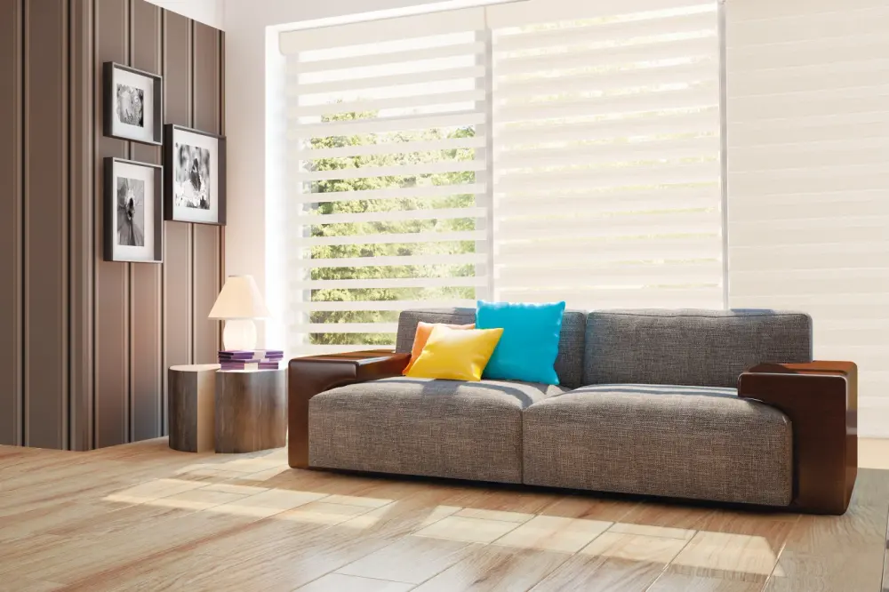 A modern living room with layered zebra shades, a gray sofa with colorful accent pillows, striped wall panels, and light wood flooring.