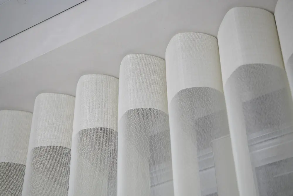 A close-up view of the top section of sheer, white ripplefold drapery.