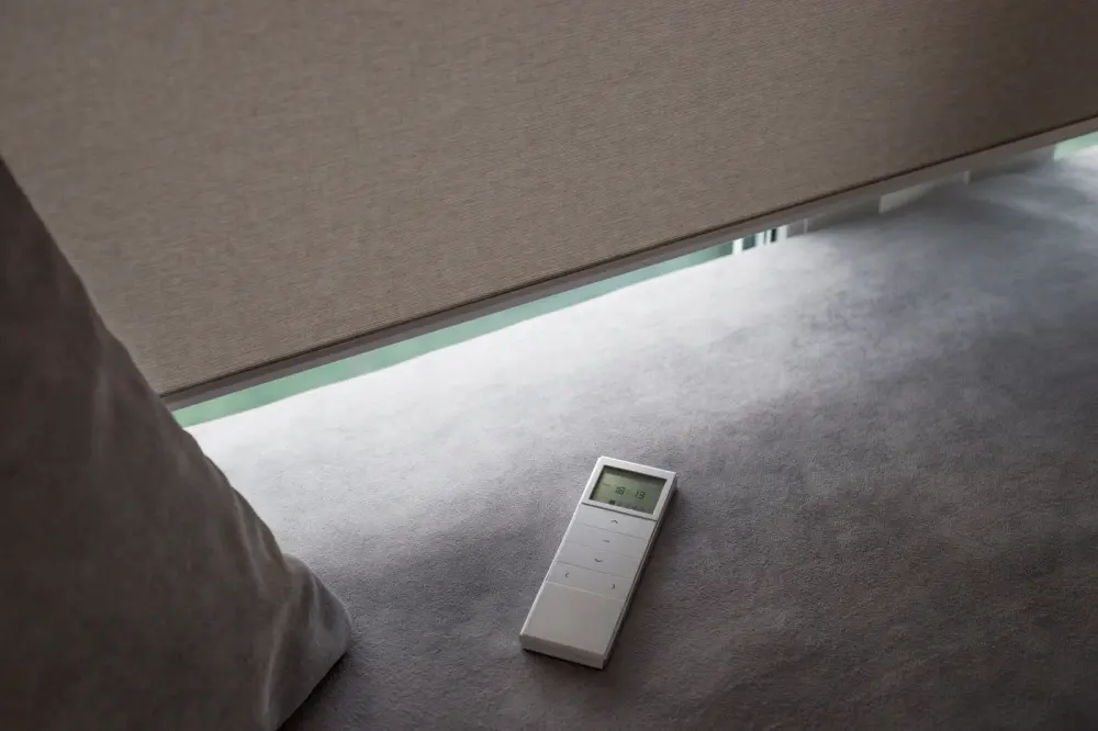 A remote for a motorized window shade sitting on a window seat below the shade.
