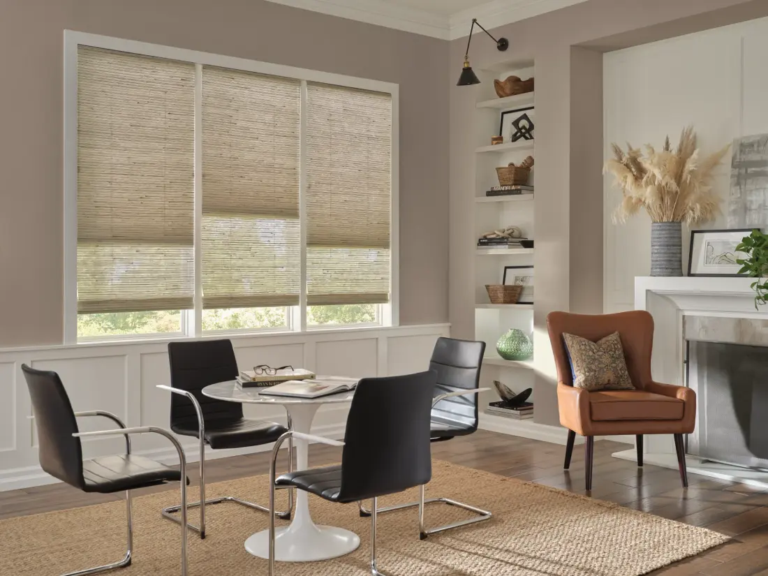 Modern living room with natural woven wood shades, black dining chairs, white round table, leather accent chair, built-in shelving, fireplace, and warm sunlight.