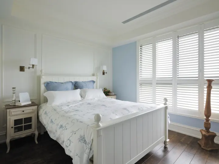A bedroom with a pale blue accent wall and indoor shutters over the windows.