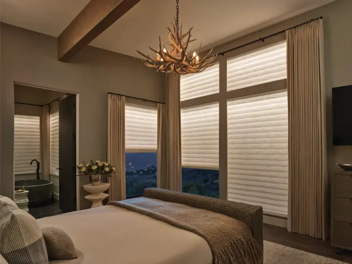 A bedroom with motorized shades covering the windows at different heights.
