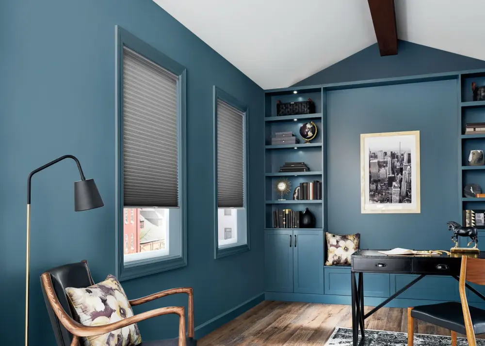 A home office with vibrant teal paint and motorized shades on the windows.