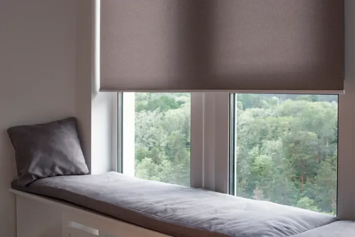 A window seat with a gray cushion and pillow backed by a gray automatic window shade.