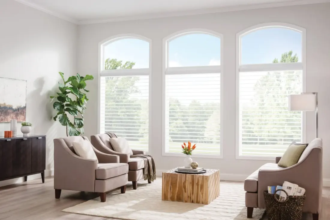 A sitting room with three large windows covered with sheer shades.
