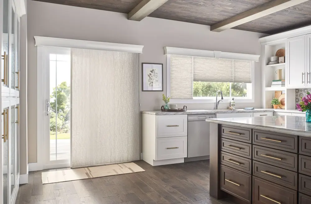 A kitchen with a patio door with shades and roller shades over the windows.