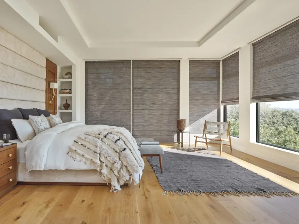 A bedroom with multiple tall windows dressed with gray Roman shades.