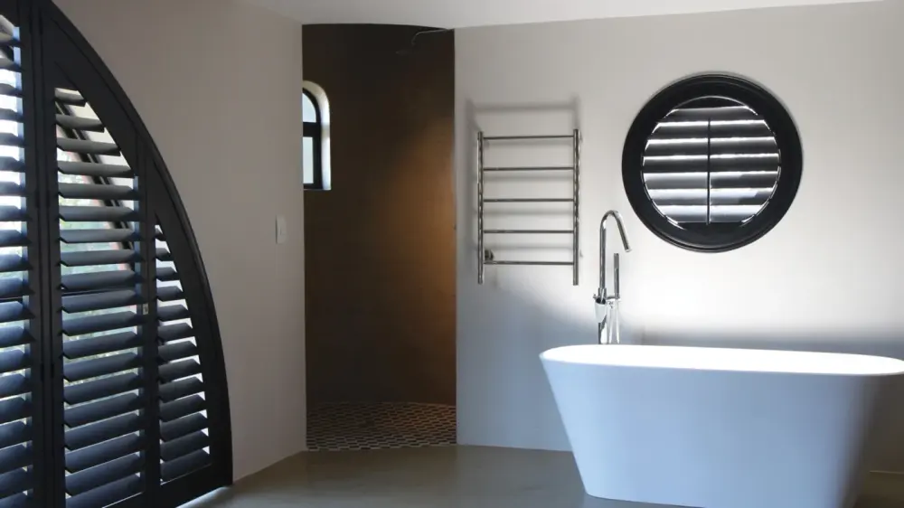 Darkened bathroom with white bathtub, white interior, with black custom-fit shutters