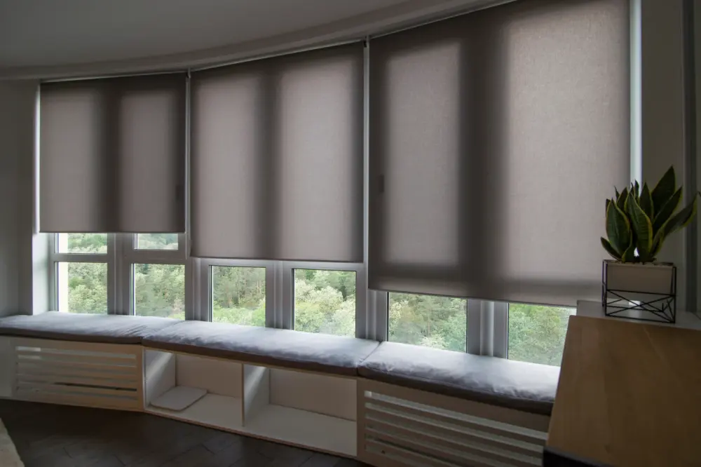 A row of windows with a long window seat and automatic window shades over the windows.