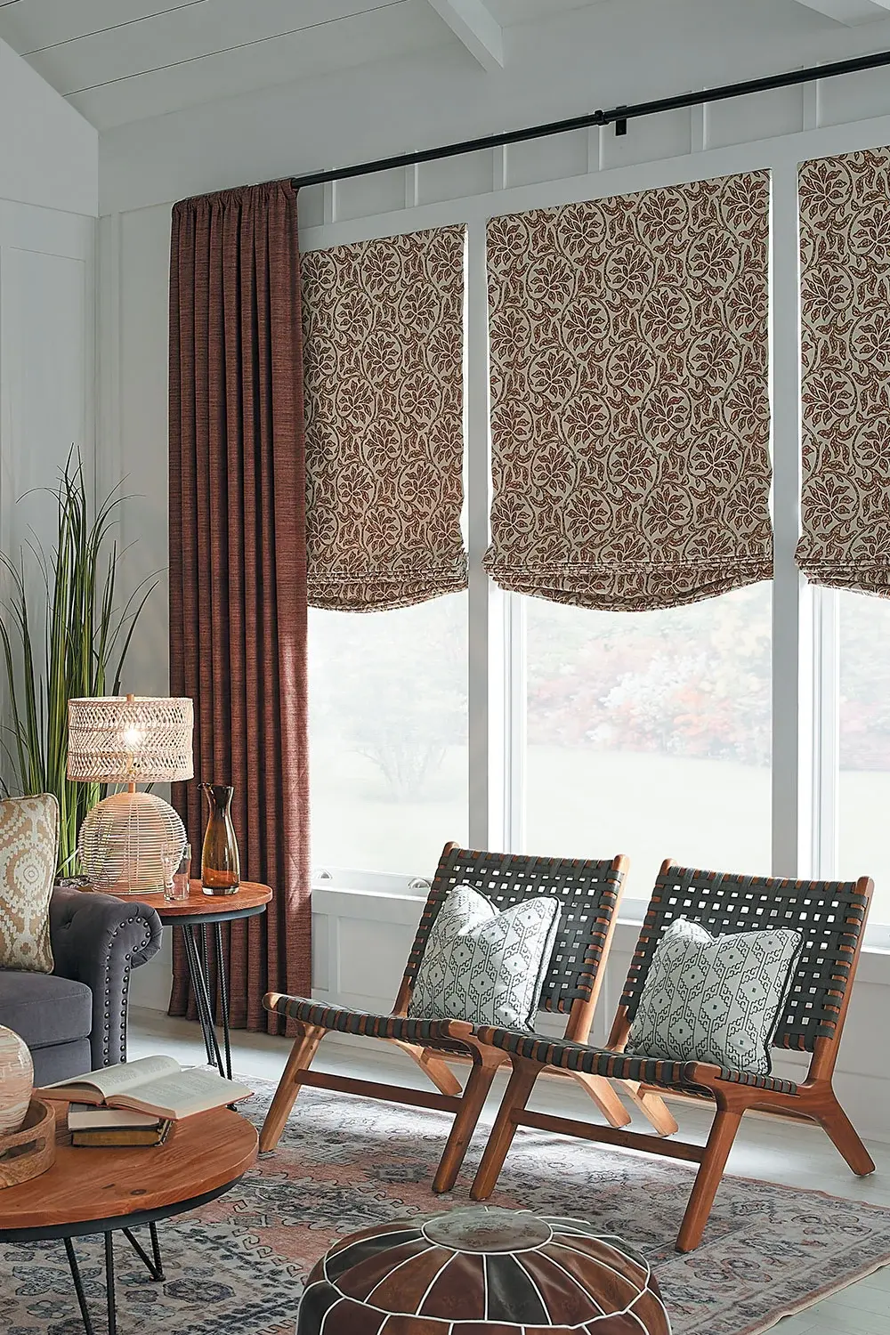 A sitting room with two chairs seated in front of the window with open reddish-brown drapery.