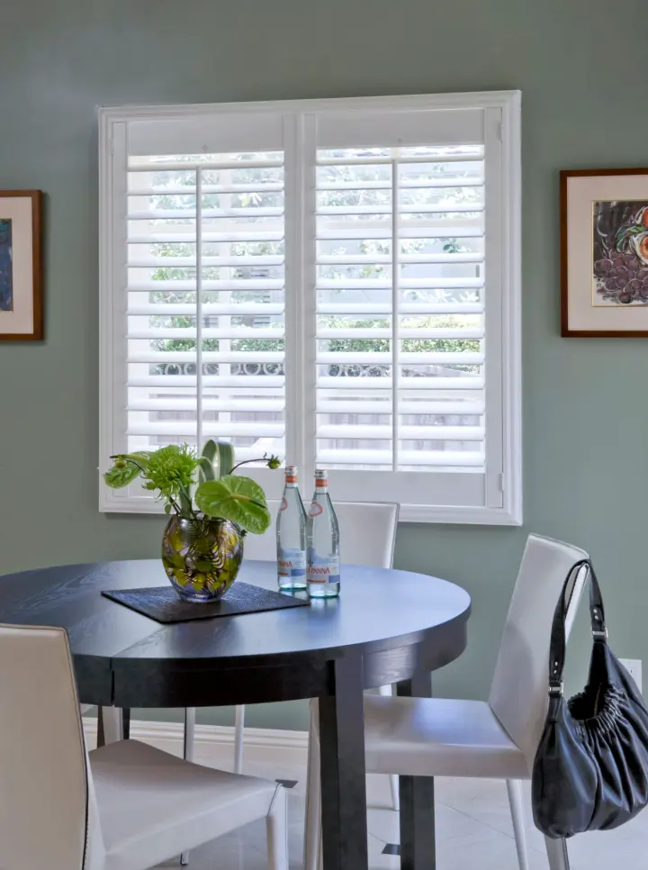 A set of white shutters allows light into an intimate dining room.