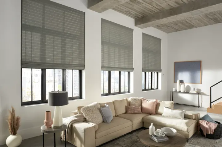 A living room with a large beige sofa with multiple pillows sitting in front of a row of windows covered by custom window shades.