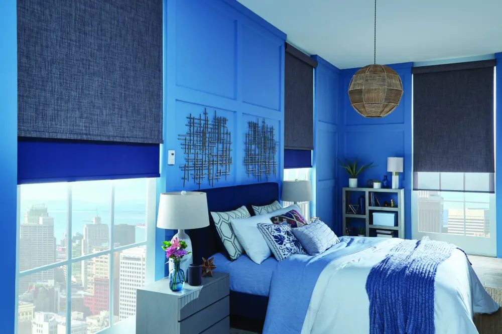 A bedroom with blue walls and denim-colored roller shades over the windows.