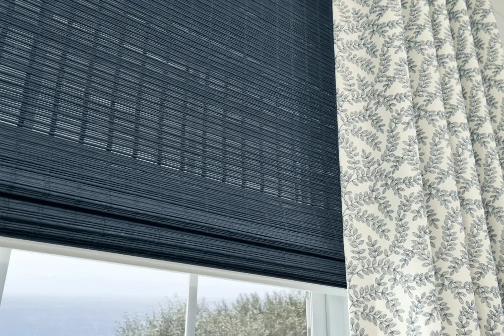 A double-layered window treatment with black woven wood shades and brown drapery.