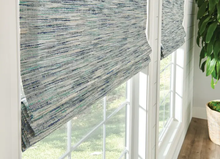 A pair of large windows in a bedroom is covered with woven wood shades. The shades are light tan in color, and they're lowered about two-thirds of the way.