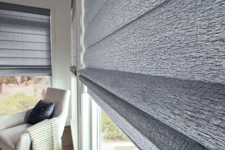 A large, floor-to-ceiling window with a black frame that overlooks a home's backyard. There are stones, cacti, and an in-ground pool visible. The window has a single-panel roller shade in light gray that is partially closed.