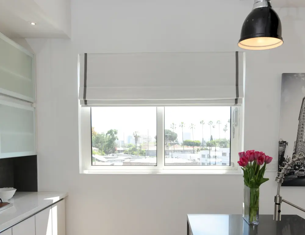 A small kitchen window with white Roman shades over it.