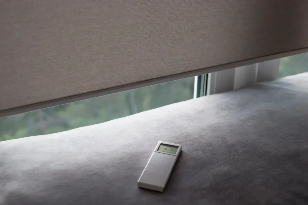 Closed motorized shade with remote on top of pillow nearby in Las Vegas, NV home | Southwest Blinds & Shutters